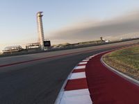 an empty racetrack with the view of a tower in the distance and green grass to the left