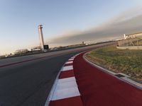 an empty racetrack with the view of a tower in the distance and green grass to the left