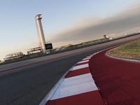 an empty racetrack with the view of a tower in the distance and green grass to the left