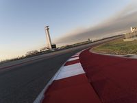 an empty racetrack with the view of a tower in the distance and green grass to the left