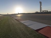 the sun is setting on the track as the grass grows in front of the runway