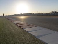 the sun is setting on the track as the grass grows in front of the runway