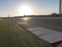 the sun is setting on the track as the grass grows in front of the runway