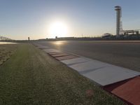 the sun is setting on the track as the grass grows in front of the runway