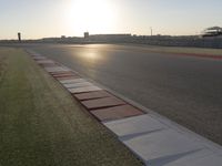 the sun is setting on the track as the grass grows in front of the runway