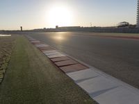 the sun is setting on the track as the grass grows in front of the runway