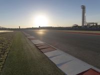 the sun is setting on the track as the grass grows in front of the runway