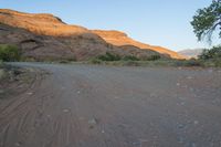 the road runs through a desert area with mountains in the distance behind it and there is a lone person standing on the path