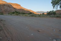 the road runs through a desert area with mountains in the distance behind it and there is a lone person standing on the path