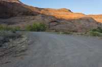 the road runs through a desert area with mountains in the distance behind it and there is a lone person standing on the path