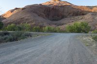 the road runs through a desert area with mountains in the distance behind it and there is a lone person standing on the path