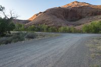 the road runs through a desert area with mountains in the distance behind it and there is a lone person standing on the path