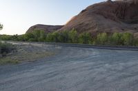 the road runs through a desert area with mountains in the distance behind it and there is a lone person standing on the path