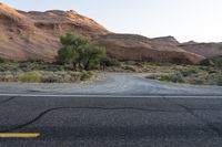 the road runs through a desert area with mountains in the distance behind it and there is a lone person standing on the path