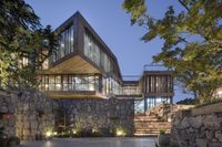 modern house made from stone and glass overlooking a pond surrounded by greenery in rural area