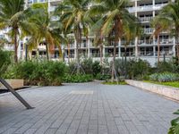 a park is next to a large modern building with many palm trees and plants surrounding it