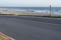 an empty road near a beach and waves as well as cars on the sand and houses on the beach