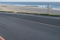 an empty road near a beach and waves as well as cars on the sand and houses on the beach