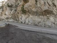 a motorcycle is riding along the side of a steep mountain road with rocks and evergreens