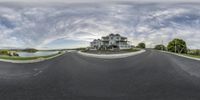 a fish - eye shot shows an empty, curving road leading to a two story house with water view in the background