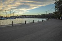 a road near a body of water at sunset with small boats in the distance along side