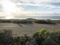 a man riding a motor bike down the road near a beach and ocean and a hill