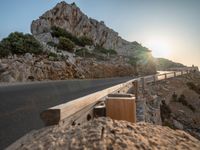 the sun setting in front of a mountain side drive line and road, and wooden railings