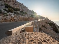 the sun setting in front of a mountain side drive line and road, and wooden railings