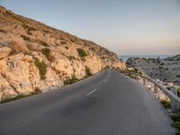 the curved road goes along the beach to a cliff shore at dusk on a clear, calm day