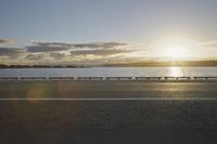 the sun shines over the water near a roadway with benches on the side of the road