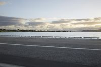 the sun shines over the water near a roadway with benches on the side of the road