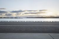 the sun shines over the water near a roadway with benches on the side of the road