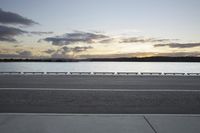 the sun shines over the water near a roadway with benches on the side of the road