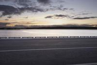 the sun shines over the water near a roadway with benches on the side of the road