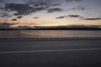 the sun shines over the water near a roadway with benches on the side of the road