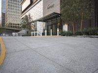 a paved parking lot with buildings and trees next to it in the background by a sidewalk