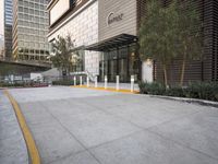 a paved parking lot with buildings and trees next to it in the background by a sidewalk