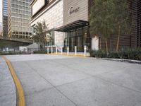 a paved parking lot with buildings and trees next to it in the background by a sidewalk