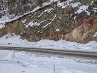 a long road that runs up a snow covered slope with a rock face in the background