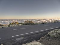 a road next to the mountain, above some clouds and in front of a highway sign