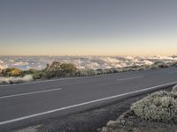 a road next to the mountain, above some clouds and in front of a highway sign
