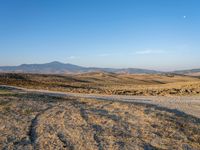 a motorcycle is parked in the desert beside a road while others sit by it on a hillside