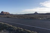 an empty dirt road leading to a desert scene, with tall trees, a mountain, and hills in the distance