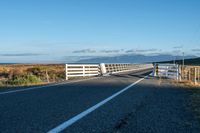 a rural road is pictured next to the ocean on a clear day with no clouds in sight