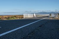 a rural road is pictured next to the ocean on a clear day with no clouds in sight