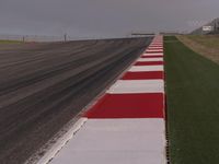 this is a runway in the countryside with a red and white stripe between it and some grass in the background
