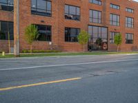 an empty street in front of a large red brick building on the other side of the road is a street light that has a line for motorists