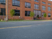 an empty street in front of a large red brick building on the other side of the road is a street light that has a line for motorists