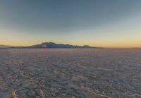 a wide picture of a snowy plain surrounded by mountains and desert land at sunrise time