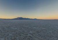 a wide picture of a snowy plain surrounded by mountains and desert land at sunrise time